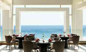 En modern restaurang med utsikt över havet, möblerade med runda bord och bekväma stolar. (AI-genererad text)