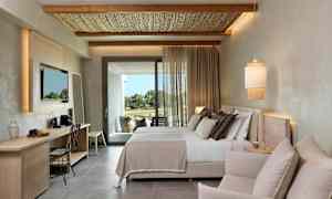 Ett modernt hotellrum med en dubbelsäng, en sittgrupp och ett skrivbord. Tyg för in dagsljus från altanutgången. (AI-genererad text)