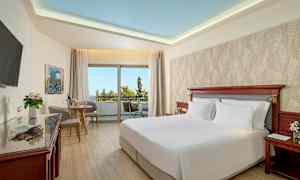 Ett hotellrum med en dubbelsäng, sittgrupp och stor balkong med utsikt. (AI-genererad text)