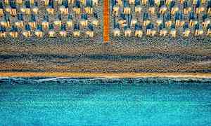 Flygfoto över en strand med parasoller och solstolar, med havet i förgrunden. (AI-genererad text)