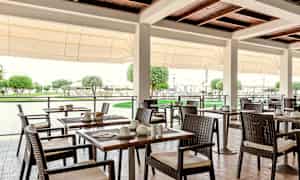 Utomhusrestaurang med bord och stolar, med grönskande omgivning. (AI-genererad text)