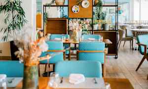 Ett modernt inrett restaurangområde med bord, turkosa stolar och dekorativa växter. (AI-genererad text)