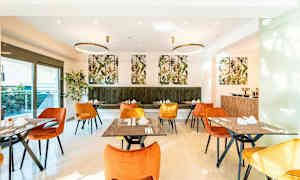 En matsal med orange och gula stolar samt grön stoppad bänk. Bord är dukade och dekorerade. Väggar har bilder av växter. (AI-genererad text)