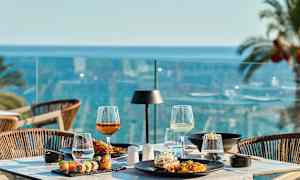 En dukad bord med mat och dryck på en terrass med utsikt över havet. (AI-genererad text)
