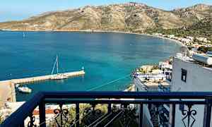 Ett balkongräcke med utsikt över en liten hamn och ett kustlandskap med berg. (AI-genererad text)