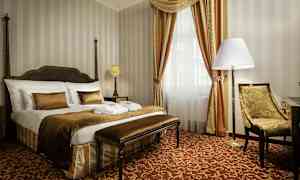 Ett elegant hotellrum med en stor säng, stol och fönster med draperier. (AI-genererad text)