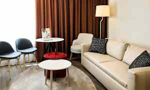 Ett vardagsrum med en ljus soffa, ett runt bord, två stolar och bruna gardiner. (AI-genererad text)