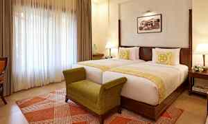 Ett hotellrum med två separata sängar, en grön bänk, och en ljus fönstergardin. (AI-genererad text)