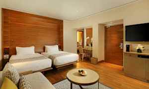 Ett modernt hotellrum med två separata sängar, ett skrivbord med en spegel, en soffa och ett litet bord. (AI-genererad text)