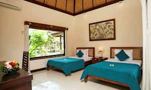 Ett ljust och stilrent inrett sovrum med två sängar med blå överkast. Ett stort fönster släpper in naturligt ljus och visar grönska utomhus. Ett fruktfat står på bordet, och en målning hänger på väggen. (AI-genererad text)