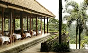 En utomhusrestaurang med halmtak och dukade bord, omgiven av frodig grönska. (AI-genererad text)