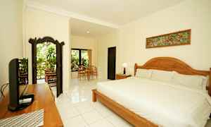 Ett väldesignat och ljust sovrum med en stor säng, trädetaljer och sittgrupp nära fönster med utsikt över grönska. (AI-genererad text)