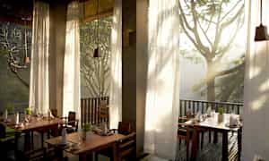 Ett ljust och luftigt restaurangutrymme med höga fönster som släpper in naturligt ljus samt utsikt över omgivande träd. (AI-genererad text)