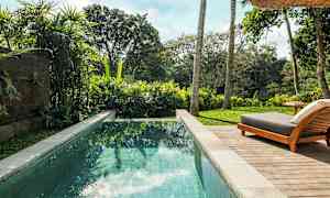 Bild av en pool med klart vatten omgiven av grönskande vegetation och en solstol på en träaltan. (AI-genererad text)