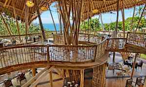 Byggnad med bambukonstruktion och möbler, med utsikt över grönska och havet. (AI-genererad text)