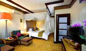 Ett hotellrum med en stor säng med vit baldakin, sittgrupp med två fåtöljer och ett bord, en TV på ett skåp och en orkidédekoration bredvid. (AI-genererad text)