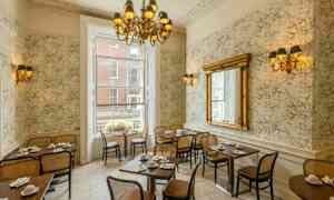 En restauranginteriör med klassisk inredning, bord och stolar, stor spegel och en ljuskrona. (AI-genererad text)