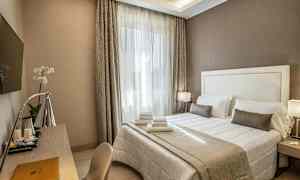 Ett hotellrum med en dubbelsäng täckt med vita och beige sängkläder, ett skrivbord med en lampa och en väggmonterad TV. (AI-genererad text)