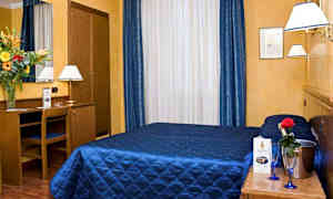 Ett hotellrum med gult väggar, blå överkast, och en byrå med spegel samt blommor på. (AI-genererad text)