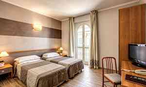 Ett hotellrum med två enkelsängar, en skrivbordshörna och ett stort fönster som släpper in dagsljus. (AI-genererad text)