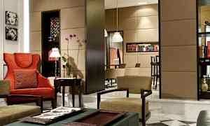 Ett elegant möblerat vardagsrum med röda och begie stolar, blommor och hyllor med böcker. (AI-genererad text)