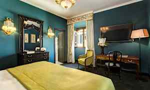 Ett elegant inrett hotellrum med grön täcke, skrivbord, spegel och gardiner framför ett öppet fönster. (AI-genererad text)