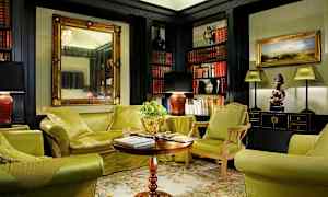 Ett elegant inrett vardagsrum med grönklädda möbler, ett soffbord och bokhyllor fyllda med böcker. (AI-genererad text)