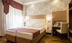 Ett hotellrum med en dubbelsäng, skrivbord och stol, samt dekorativa detaljer. (AI-genererad text)