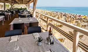 En restaurang med dukade bord nära en strand med parasoller och solstolar. (AI-genererad text)