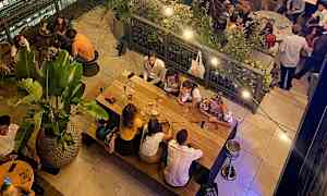 En restaurang med människor som sitter vid bord och äter i en avslappnad miljö. (AI-genererad text)