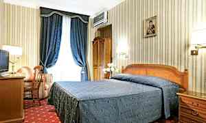 Ett hotellrum med en dubbelsäng klädd i blått överkast, ett skrivbord, en fåtölj och blå gardiner. (AI-genererad text)