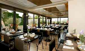 En ljus restaurang med dukade bord, dekorerade med blommor och fönster som visar en utomhusmiljö. (AI-genererad text)