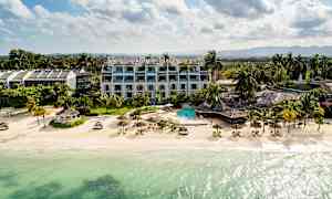 Strand med klart vatten, parasoll och solstolar, omgiven av hotell och grönska. (AI-genererad text)