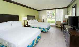 Ett hotellrum med två dubbelsängar, ett skrivbord med en TV, och stora glasdörrar som vetter mot en trädgård. (AI-genererad text)