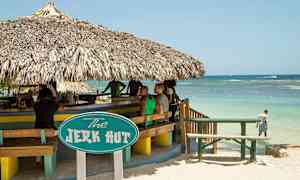 En strandbar med halmtak och en skylt som lyder "The Jerk Hut". Utsikt över havet kan ses i bakgrunden. (AI-genererad text)