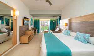 Ett hotellrum med en dubbelsäng och blåa detaljer. Det finns också en soffa, ett skrivbord och en balkong med utsikt. (AI-genererad text)