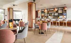 Ett modernt inrett café eller bar med bord och stolar av olika färger samt en upplyst bardisk i bakgrunden. (AI-genererad text)