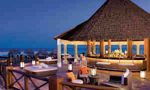 Avslappnad lounge och bar med tak i halm, vid stranden vid skymning. (AI-genererad text)