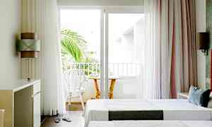 Ljusa hotellrum med två enkelsängar och en balkong med stolar samt ett bord. (AI-genererad text)