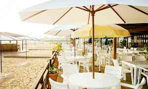 En strandbar med parasoller och vita bord och stolar. (AI-genererad text)