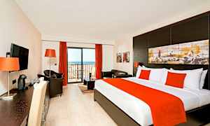 Ett hotellrum med säng, sittgrupp och balkongsdörr. (AI-genererad text)