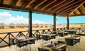 Restaurang med uteservering och utsikt över en strand med solstolar och parasoller. (AI-genererad text)