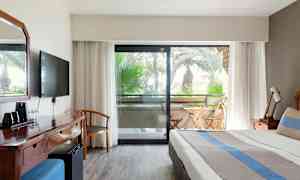 Bild av hotellrum med säng, skrivbord och balkong med utemöbler. (AI-genererad text)