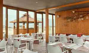 Restaurang med träpanel och glasväggar med utsikt över stranden. (AI-genererad text)