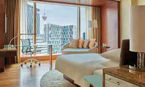 Ett modernt hotellrum med fönster som visar en utsikt över en stad, inklusive en tornstruktur. (AI-genererad text)