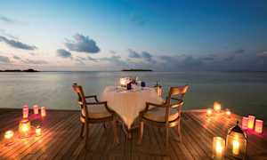 Ett bord med två stolar står på en träbrygga vid vattnet, omgivet av tända ljus. (AI-genererad text)
