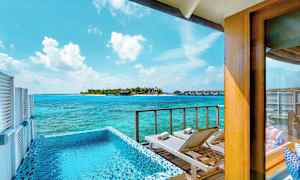 Utsikt från en terrass med pool och solstolar mot havet och en ö med bungalows. (AI-genererad text)