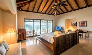 Interiör av ett sovrum med en dubbelsäng och ett öppet fönster mot en balkong. (AI-genererad text)