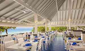 Utomhusrestaurang med vita möbler och havsutsikt. (AI-genererad text)