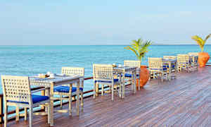 Uteservering med bord och stolar vid havet. (AI-genererad text)